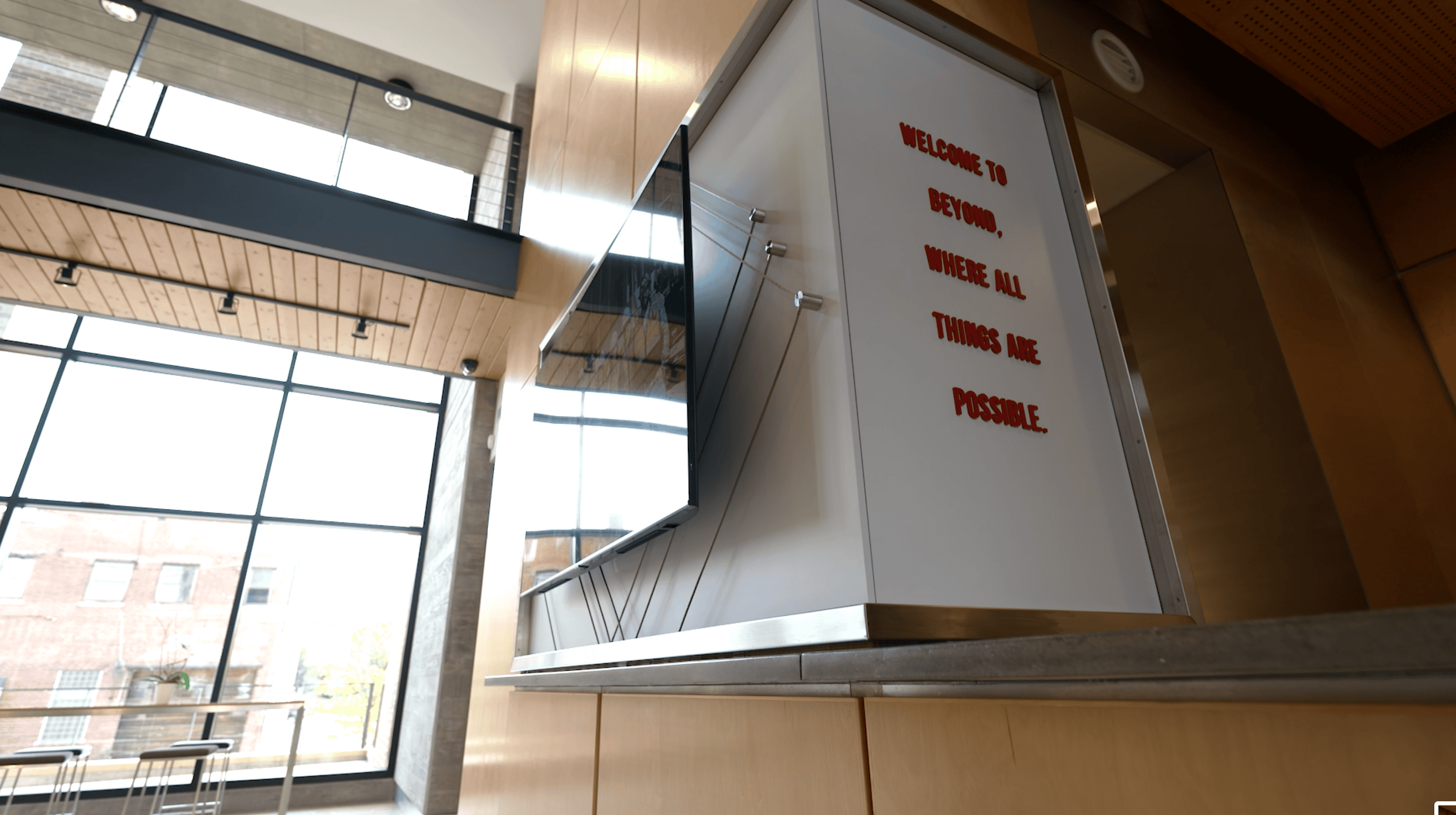 Side view of a digital display mounted in a modern office lobby, with the text 